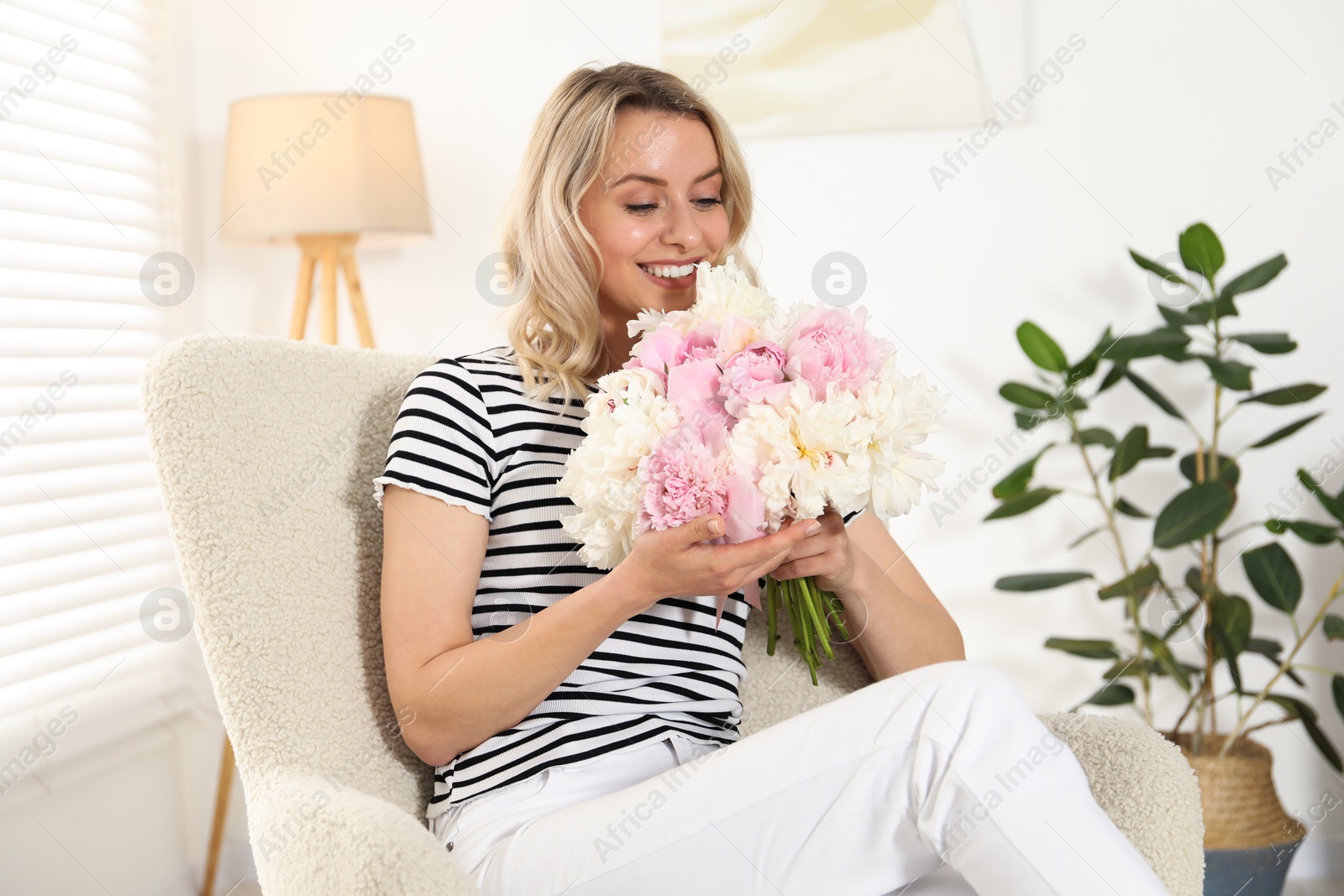 Photo of Happy woman with bouquet of beautiful peonies in armchair indoors