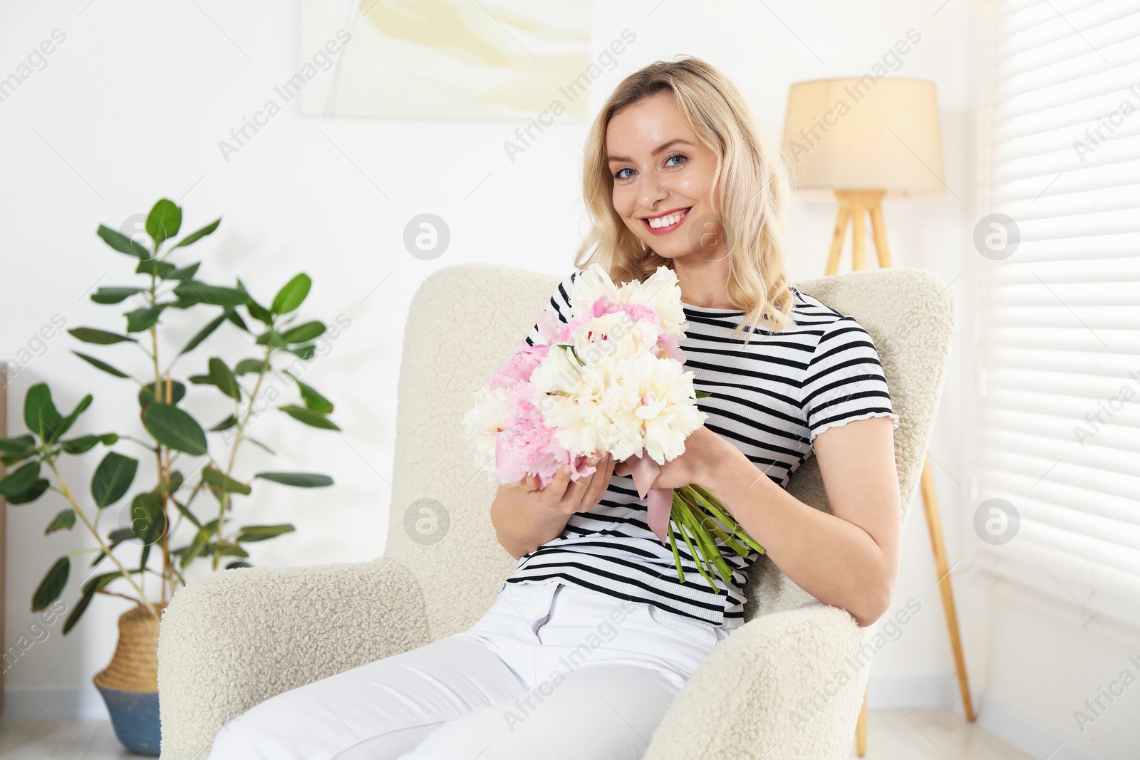 Photo of Happy woman with bouquet of beautiful peonies in armchair indoors