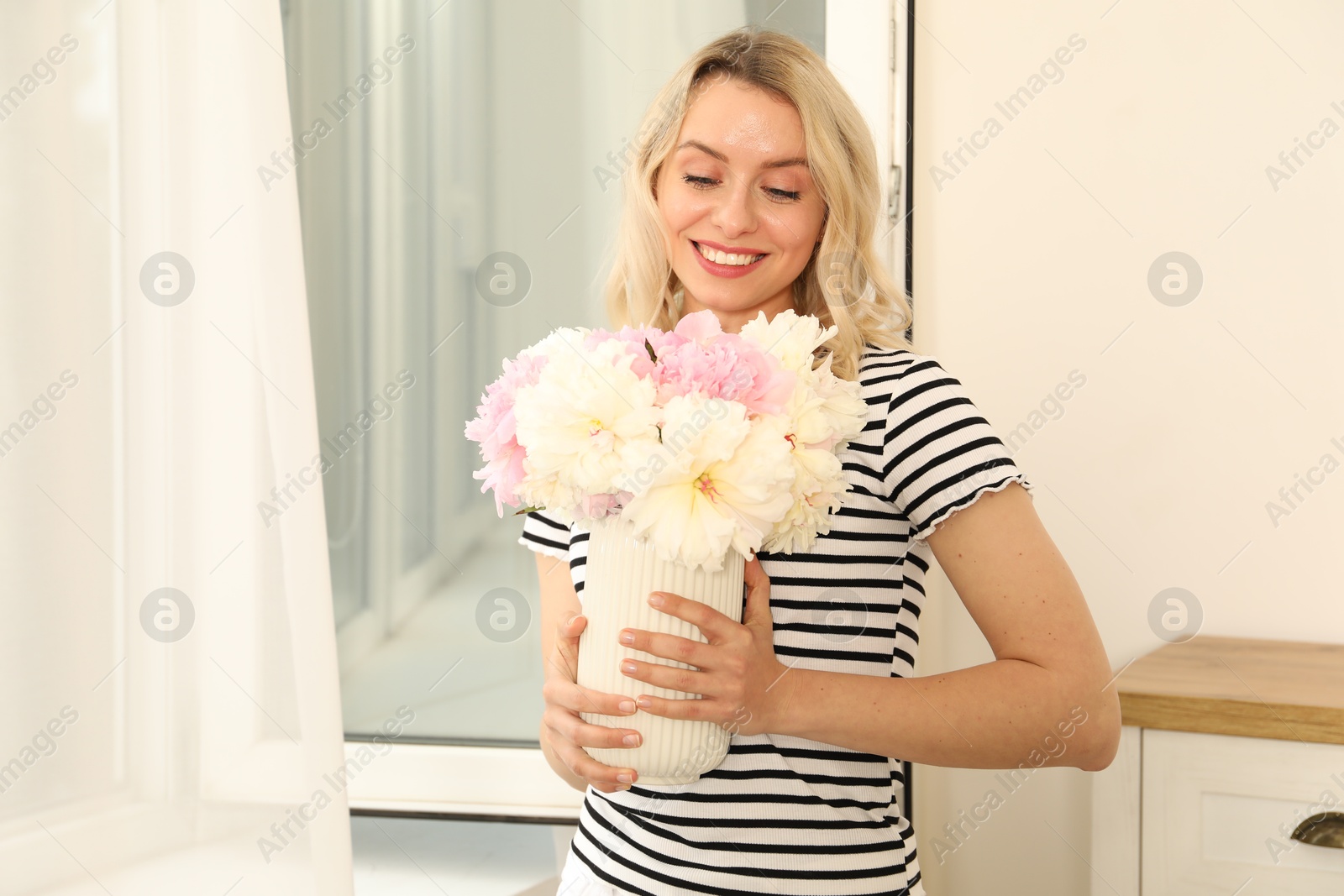 Photo of Happy woman with bouquet of beautiful peonies near window indoors