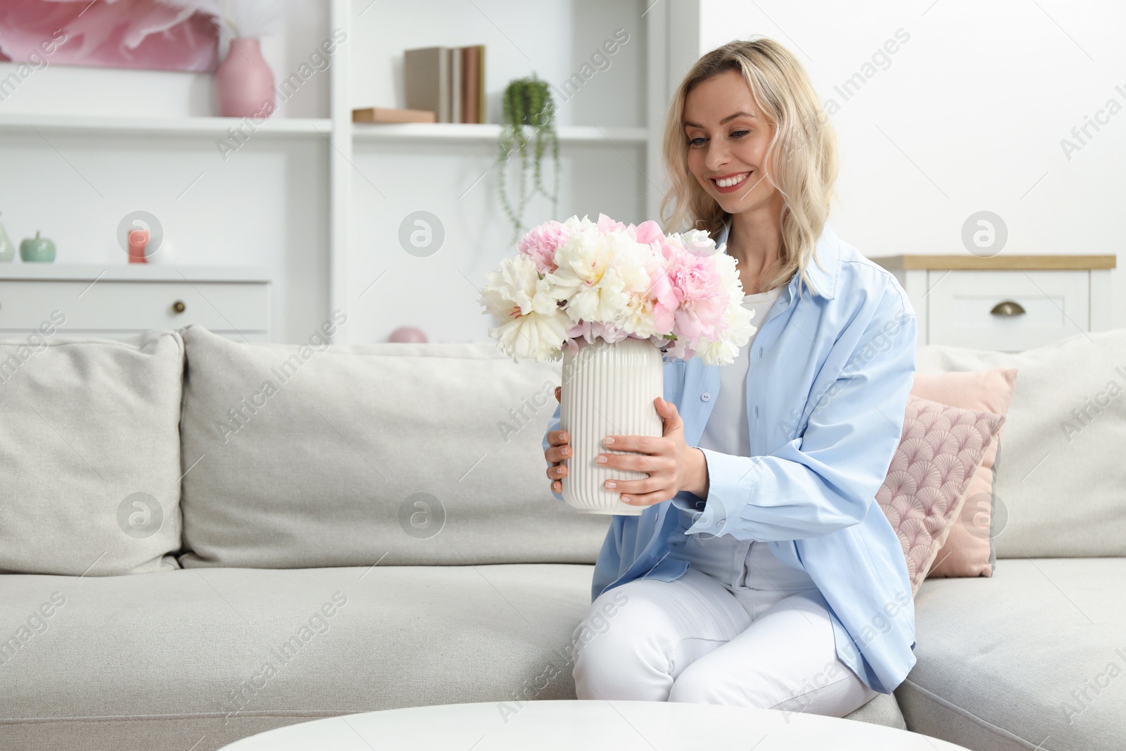 Photo of Happy woman with bouquet of beautiful peonies on sofa at home, space for text
