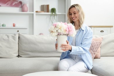 Photo of Happy woman with bouquet of beautiful peonies on sofa at home, space for text