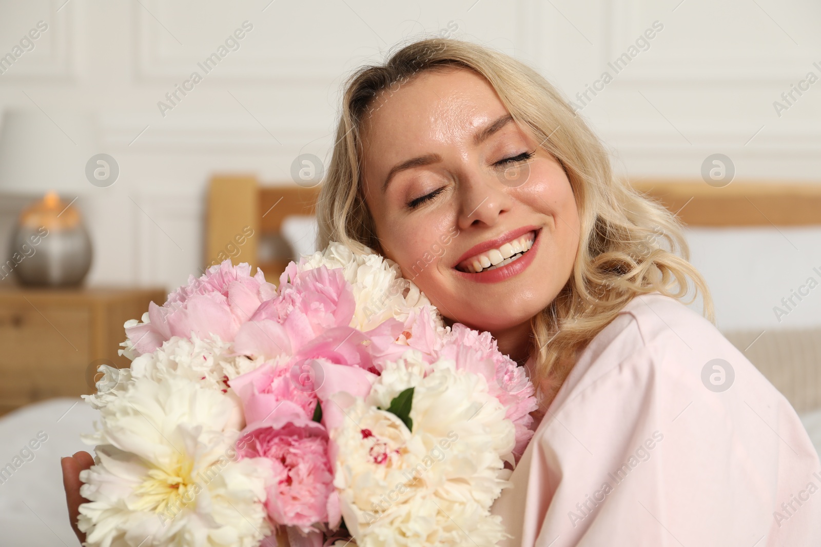 Happy woman with bouquet of beautiful peonies in bedroom Photo of Happy woman with bouquet of beautiful peonies in bedroom