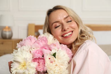 Photo of Happy woman with bouquet of beautiful peonies in bedroom