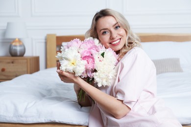 Photo of Happy woman with bouquet of beautiful peonies in bedroom