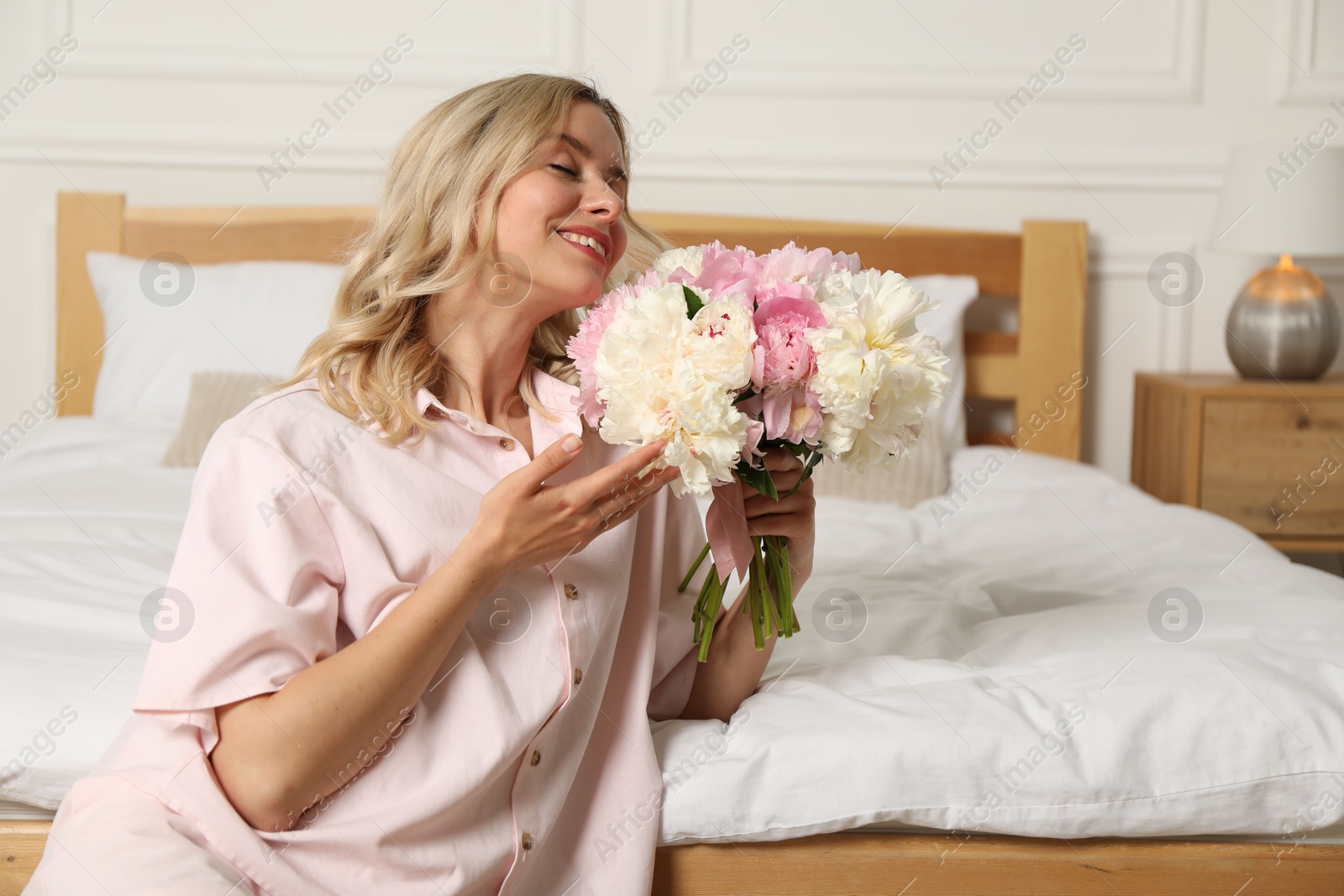 Photo of Happy woman with bouquet of beautiful peonies in bedroom