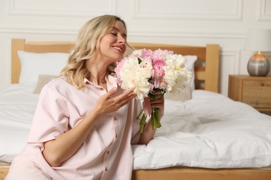 Photo of Happy woman with bouquet of beautiful peonies in bedroom