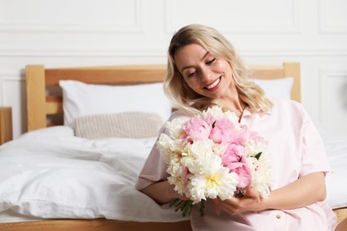 Photo of Happy woman with bouquet of beautiful peonies in bedroom, space for text