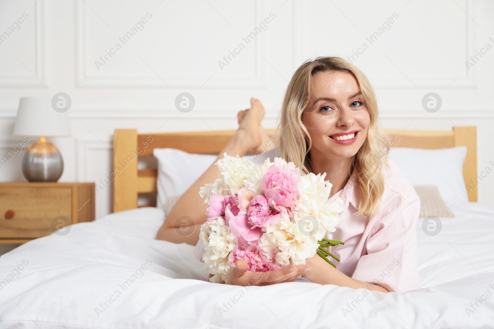 Photo of Happy woman with bouquet of beautiful peonies on bed indoors