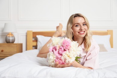Photo of Happy woman with bouquet of beautiful peonies on bed indoors