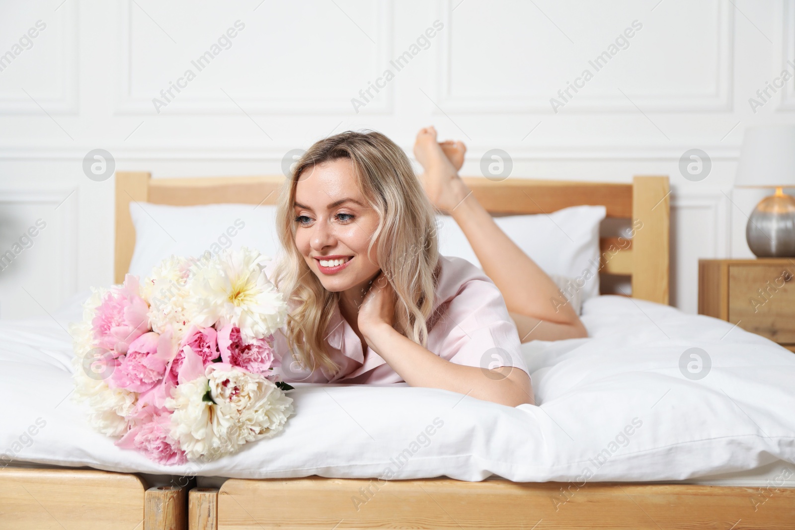 Photo of Happy woman with bouquet of beautiful peonies on bed indoors