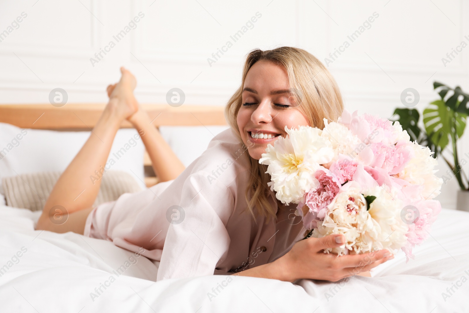 Photo of Happy woman with bouquet of beautiful peonies on bed indoors
