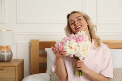 Photo of Happy woman with bouquet of beautiful peonies on bed indoors, space for text