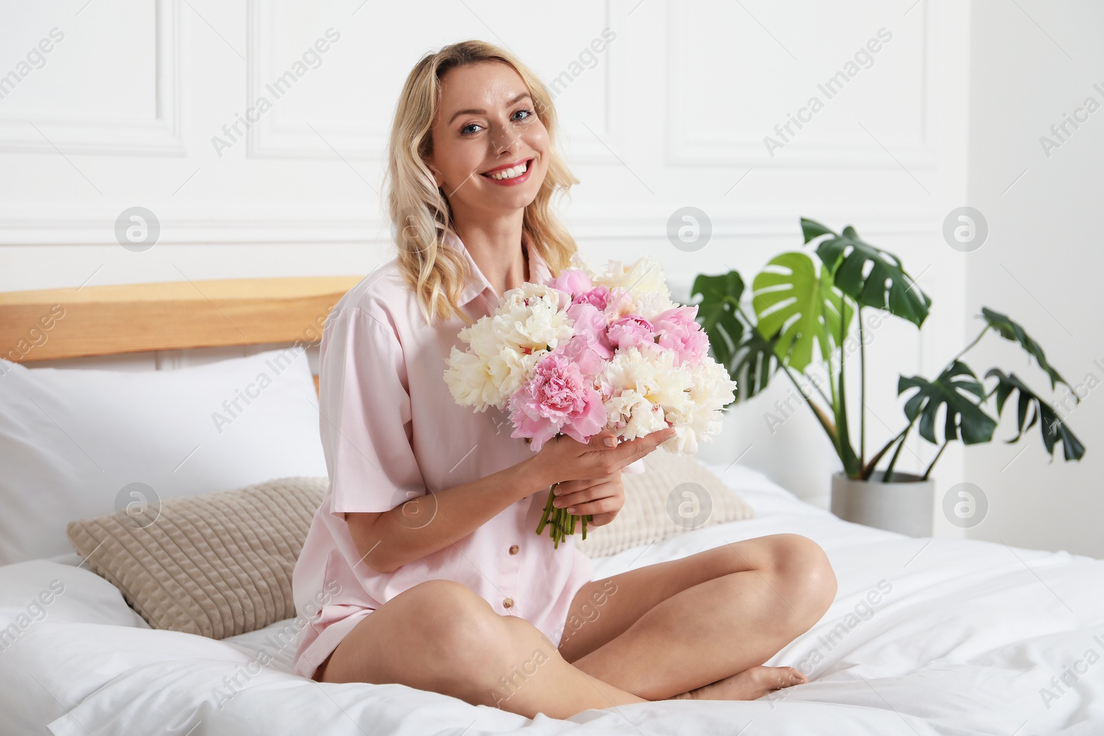 Photo of Happy woman with bouquet of beautiful peonies on bed indoors