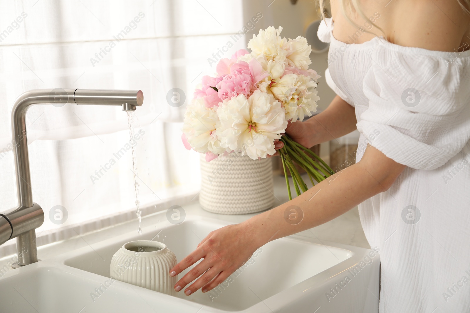 Woman taking care of beautiful peonies in kitchen, closeup Photo of Woman taking care of beautiful peonies in kitchen, closeup