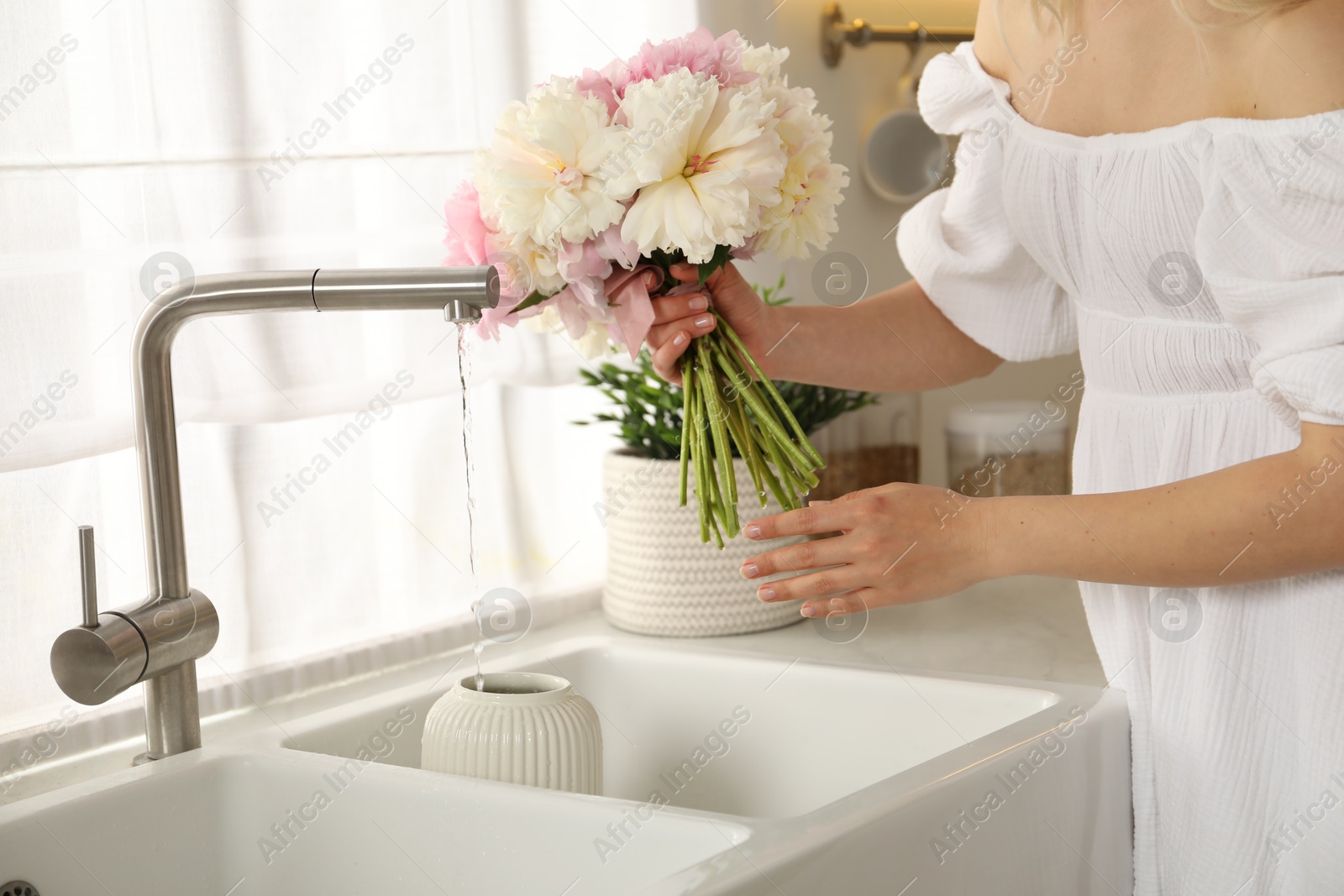 Woman taking care of beautiful peonies in kitchen, closeup Photo of Woman taking care of beautiful peonies in kitchen, closeup