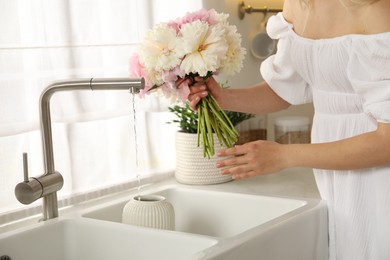 Photo of Woman taking care of beautiful peonies in kitchen, closeup
