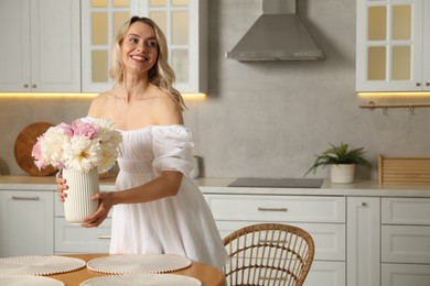Photo of Happy woman arranging vase with bouquet of beautiful peonies onto table in kitchen