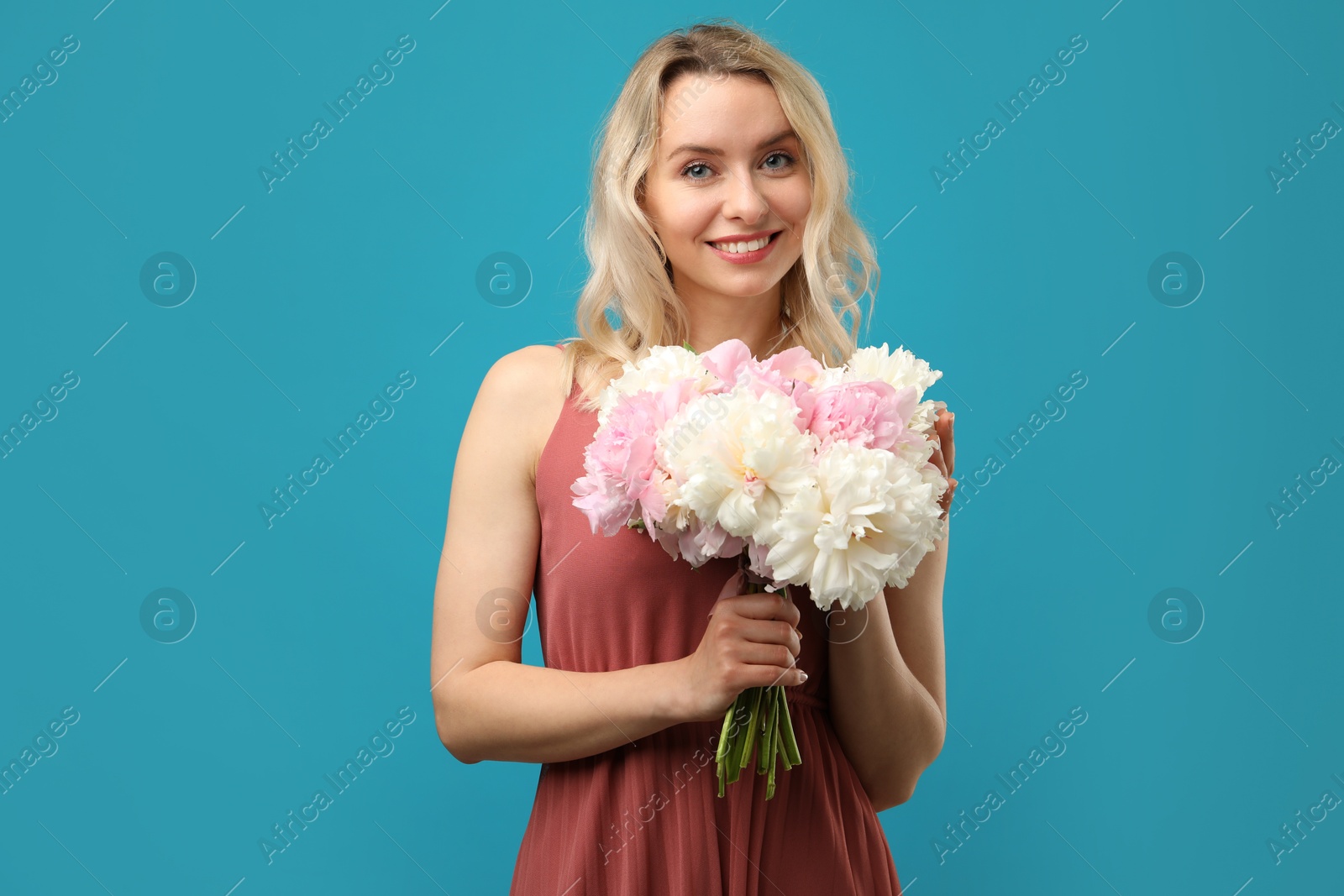 Photo of Happy woman with bouquet of beautiful peonies on light blue background