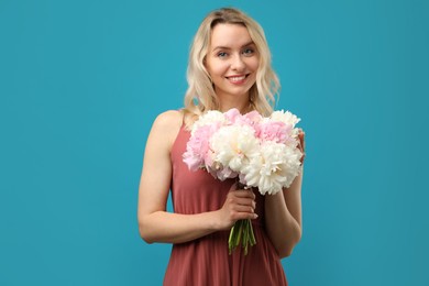 Photo of Happy woman with bouquet of beautiful peonies on light blue background