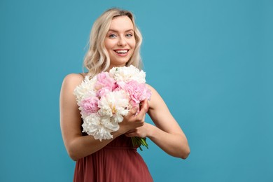 Photo of Happy woman with bouquet of beautiful peonies on light blue background