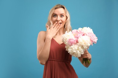 Photo of Happy woman with bouquet of beautiful peonies on light blue background