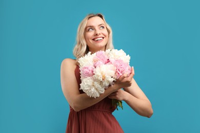 Photo of Happy woman with bouquet of beautiful peonies on light blue background