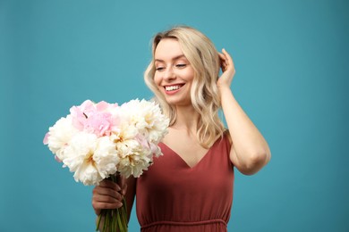 Photo of Happy woman with bouquet of beautiful peonies on light blue background