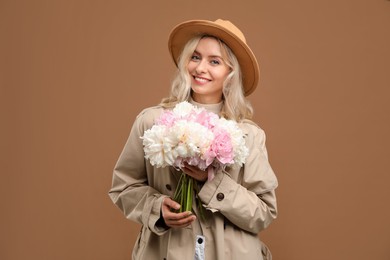 Photo of Happy woman with bouquet of beautiful peonies on brown background