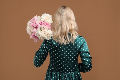 Photo of Woman with bouquet of beautiful peonies on brown background, back view