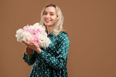 Photo of Happy woman with bouquet of beautiful peonies on brown background, space for text