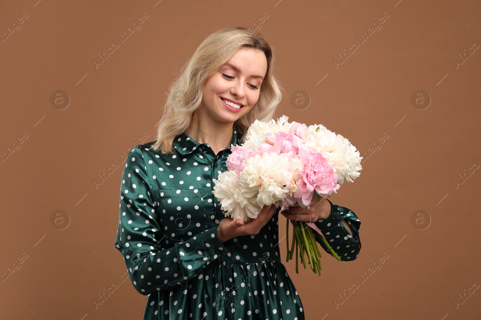 Photo of Happy woman with bouquet of beautiful peonies on brown background