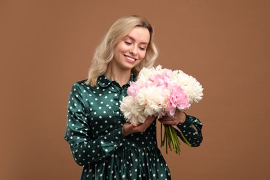 Photo of Happy woman with bouquet of beautiful peonies on brown background