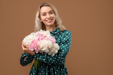 Photo of Happy woman with bouquet of beautiful peonies on brown background, space for text
