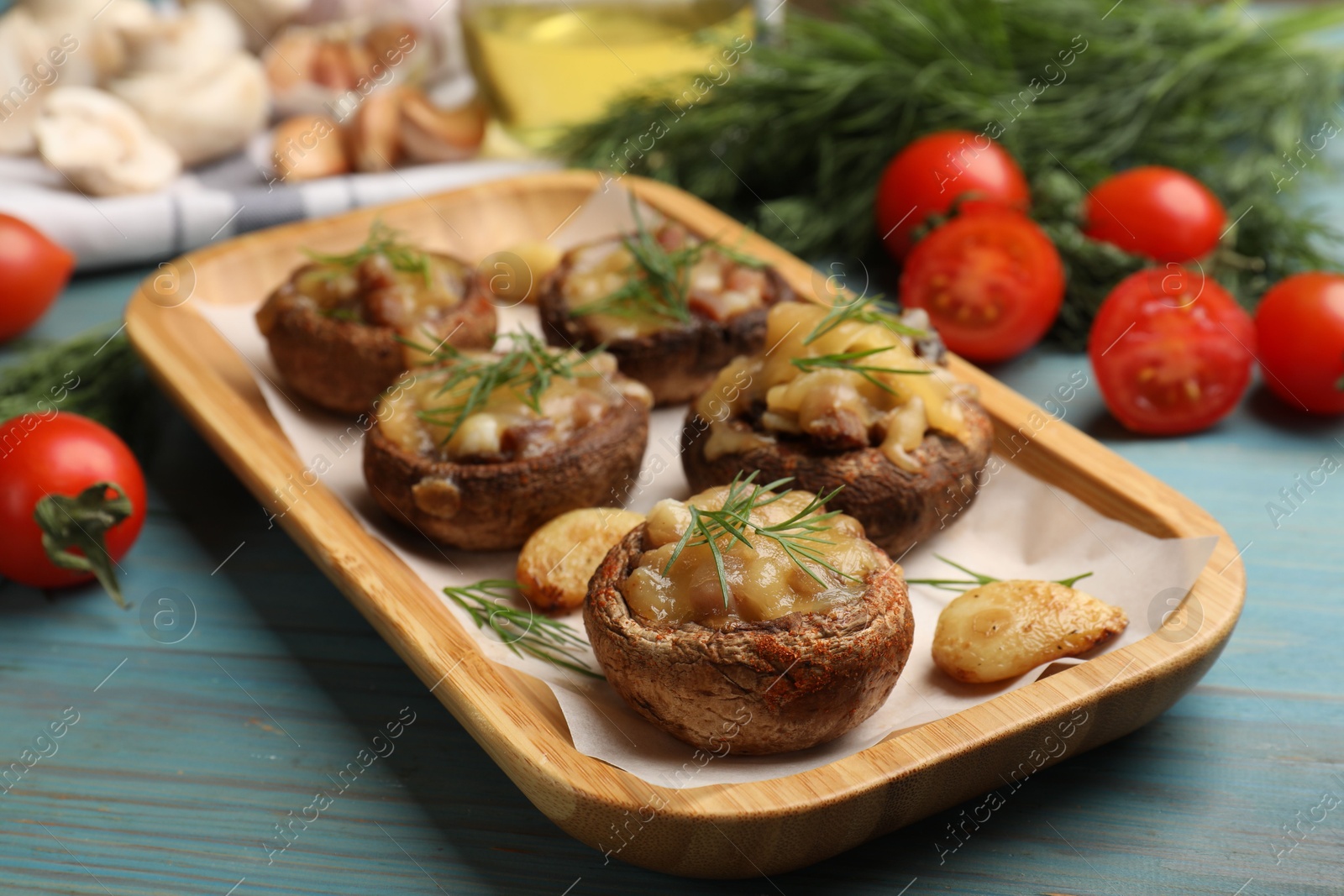 Delicious stuffed mushrooms with melted cheese, garlic and dill on light blue wooden table, closeup Photo of Delicious stuffed mushrooms with melted cheese, garlic and dill on light blue wooden table, closeup