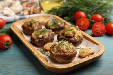 Photo of Delicious stuffed mushrooms with melted cheese, garlic and dill on light blue wooden table, closeup