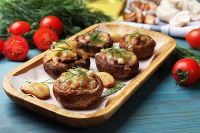 Photo of Delicious stuffed mushrooms with melted cheese, garlic and dill on light blue wooden table, closeup