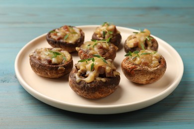 Photo of Delicious stuffed mushrooms with melted cheese and thyme on light blue wooden table, closeup