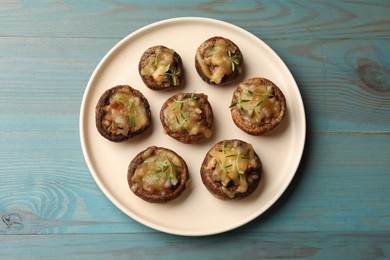 Photo of Delicious stuffed mushrooms with melted cheese and thyme on light blue wooden table, top view