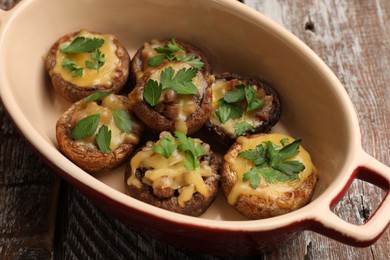 Photo of Delicious stuffed mushrooms with melted cheese and parsley in baking dish on color wooden table, closeup