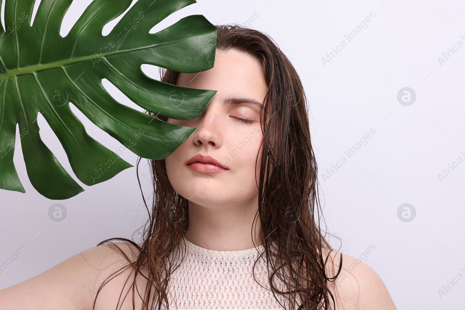 Photo of Portrait of beautiful woman with natural skin complexion and monstera leaf on grey background, closeup