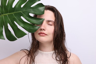 Photo of Portrait of beautiful woman with natural skin complexion and monstera leaf on grey background, closeup