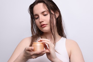 Photo of Portrait of beautiful woman with jar of skincare product on light grey background, closeup