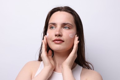 Photo of Beautiful woman applying skincare product onto her face on light grey background, closeup