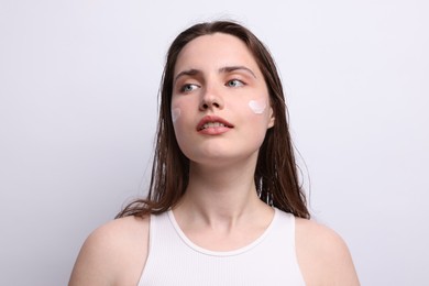 Photo of Beautiful woman with skincare product on her face against light grey background, closeup