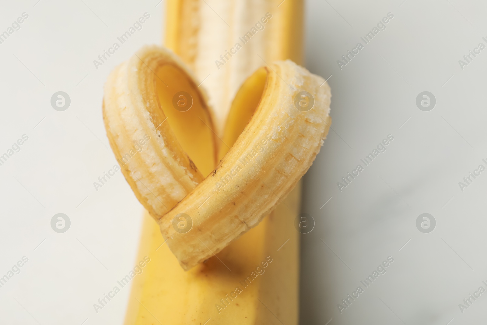 Photo of Banana with heart made of peel on white table, closeup