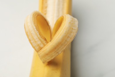 Photo of Banana with heart made of peel on white table, closeup