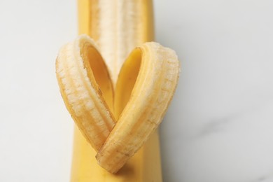 Photo of Banana with heart made of peel on white table, closeup