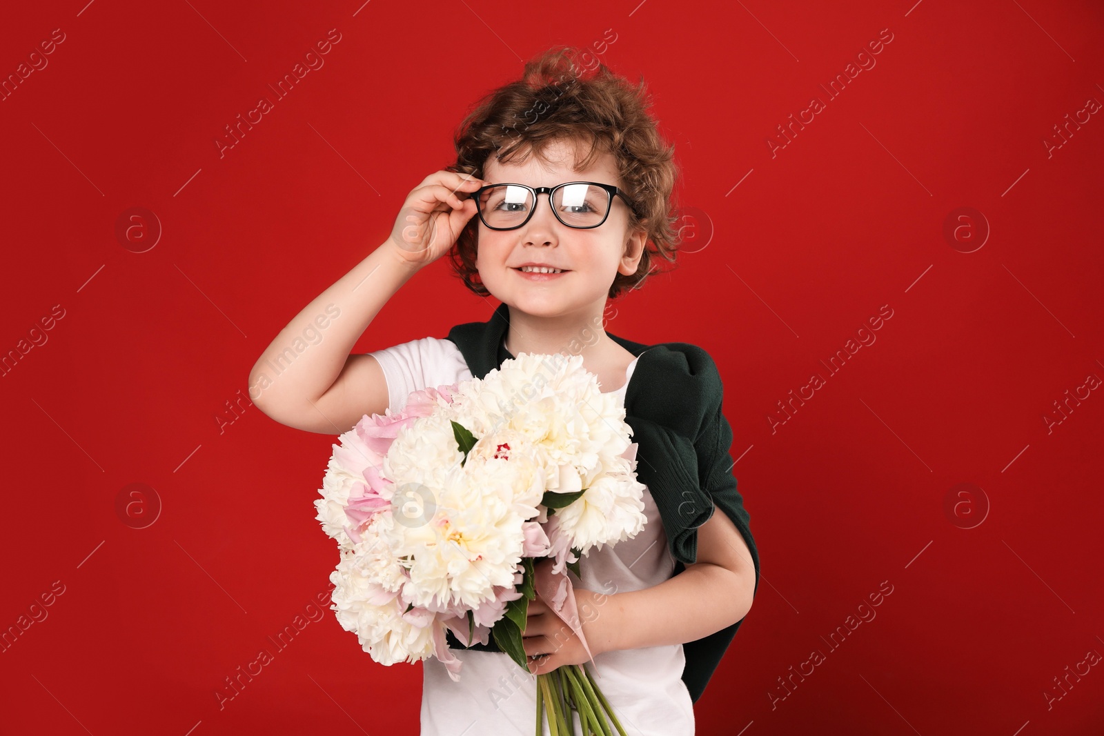 Cute little boy with bouquet of beautiful peonies on red background Photo of Cute little boy with bouquet of beautiful peonies on red background