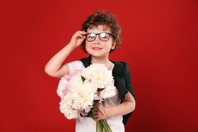 Photo of Cute little boy with bouquet of beautiful peonies on red background
