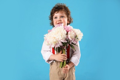Photo of Cute little boy with bouquet of beautiful peonies on light blue background